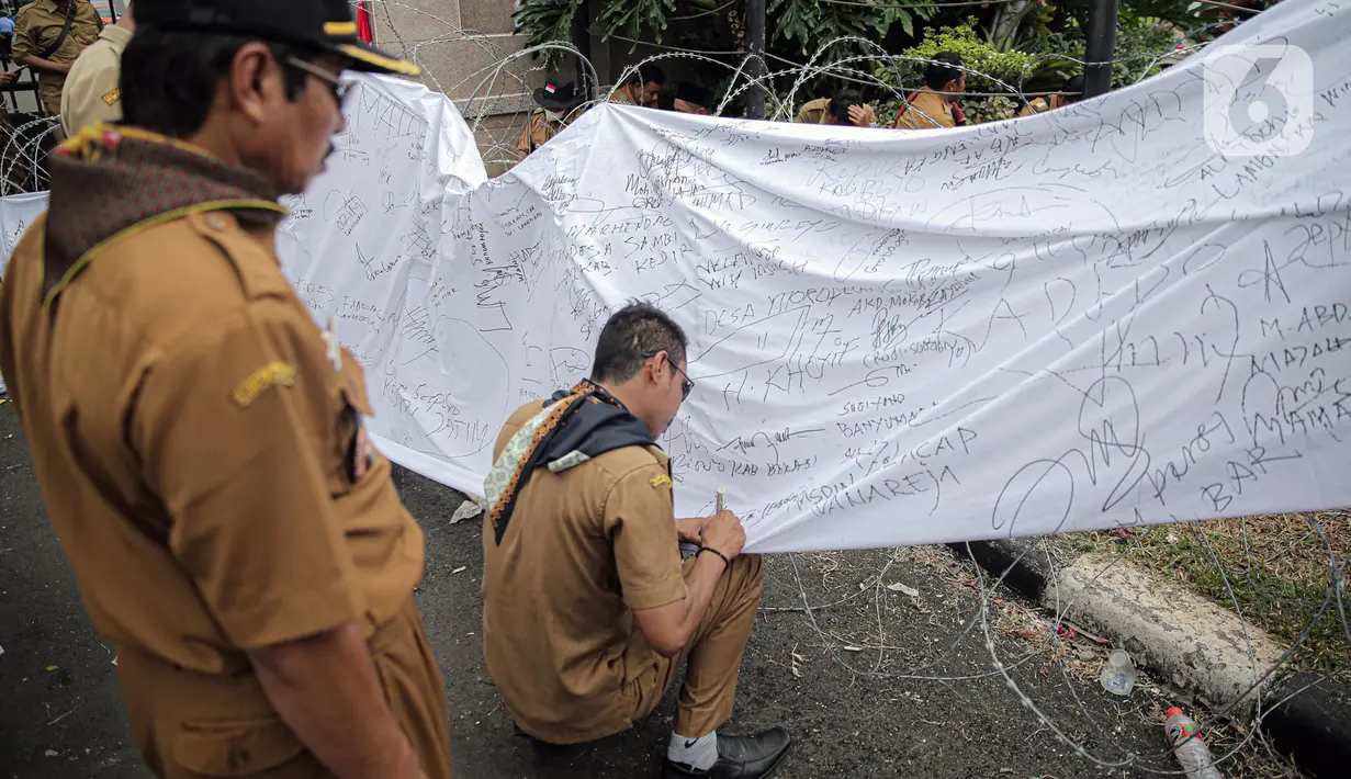 Seorang kepala desa membubuhkan tanda tangan pada spanduk saat melakukan aksi di depan Gedung DPR RI, Jakarta, Selasa (17/1/2023). Dalam aksi yang diikuti ribuan orang tersebut mereka menuntut perpanjangan masa jabatan kepala desa yang sebelumnya enam tahun menjadi sembilan tahun dan meminta DPR RI merevisi masa jabatan yang diatur dalam UU Nomor 6 Tahun 2014 tentang Desa. (Liputan6.com/Faizal Fanani)