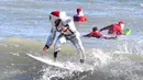 Peselancar Corey Howell yang menganakan pakaian luar angkasa serta Sinterklas berselancar untuk acara tahunan ke-14 Surfing Santas of Cocoa Beach di Cocoa Beach, Florida, Amerika Serikat, 24 Desember 2022. (Malcolm Denemark/Florida Today via AP)