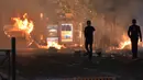 Dua orang berjalan di dekat api saat terjadi kericuhan yang disebabkan oleh pendukung Marseille di Vieux Port di Marseille, Prancis (16/5). (AFP Photo/Bertrand Langlois)