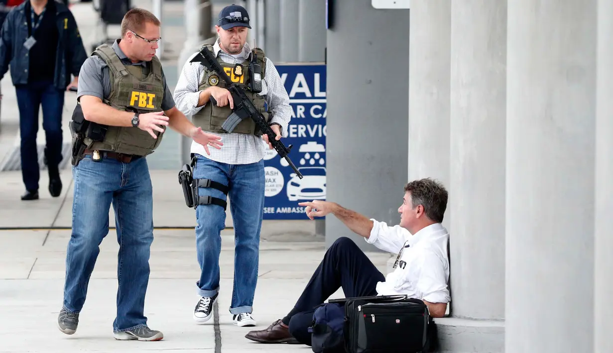 Petugas kepolisian berbincang dengan penumpang saat terjadi penembakan di Bandara Fort Lauderdale, Florida, AS (6/1). Ratusan orang dilaporkan berada di sekitar lokasi saat penembakan terjadi. (AP Photo/Wilfredo Lee)