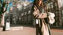 Gaya kasual Adinda Thomas saat liburan keluar negeri. Ia tampil memesona dalam balutan busana tumpuk dengan coat panjang abu-abu dan syal hitam. [Foto: Instagram/adindathomas]