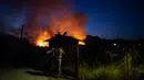 Para lelaki menutup pintu ketika api membakar di dekat desa Galataki, dekat Korintus, Yunani, Rabu, (22/7/2020). Pemerintah Yunani mengevakuasi lima pemukiman sebagai tindakan pencegahan. (AP Photo/Petros Giannakouris)
