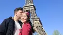 Di depan Menara Eiffel, Gracia Indri mengabadikan momen bersama sang suami mengenakan coat berwarna merah dan syal kotak-kotak berwarna senada. (instagram/graciaz14)