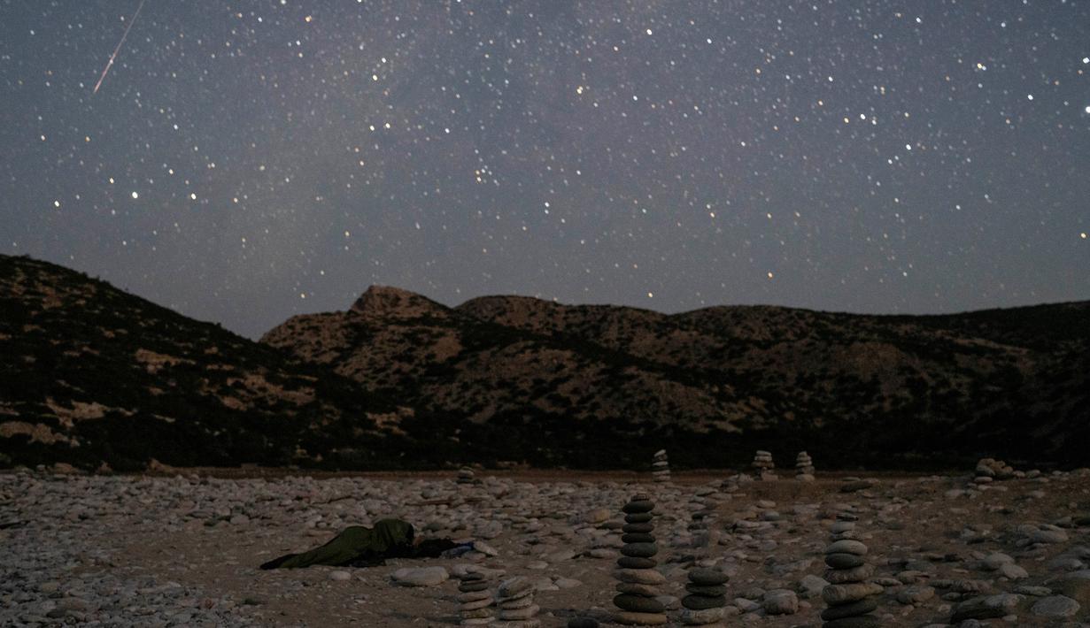Dalam foto yang diambil dengan kecepatan rana lambat ini memperlihatkan sebuah meteor Perseid memercik saat memasuki atmosfer Bumi ketika seorang pria tidur di Pantai Tripiti, Pulau Gavdos, titik paling selatan Yunani dan Eropa, Minggu (13/8/2023) dini hari. (AP Photo/Petros Giannakouris)