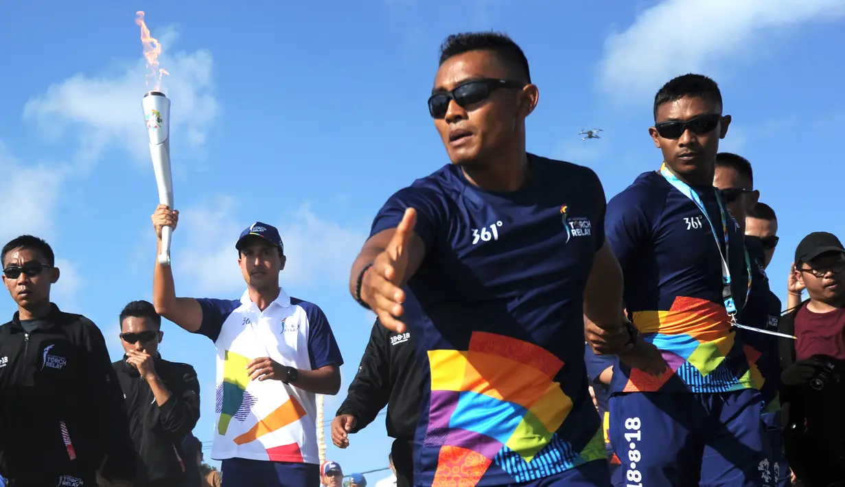 Aktor Hamish Daud (kedua kiri) membawa obor pada kirab obor Asian Games 2018 di Pantai Kuta, Bali, Senin (23/7). Torch Relay Asian Games 2018 melintasi empat kabupaten di Bali dengan arak-arakan berkeliling di sejumlah obyek wisata. (AFP/SONNY TUMBELAKA)