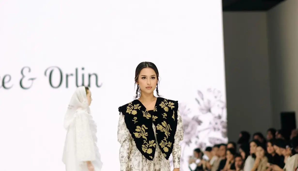 Ia tampil feminin mengenakan long dress lengan panjang warna putih dengan motif floral yang indah.
