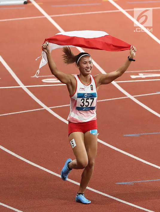 Pelari Indonesia, Nova Emilia membawa bendera merah putih usai finis di urutan kedua setelah pelari Korea Selatan Jung Hyelim pada final atletik nomor lari halang rintang 100 meter putri di Stadion Utama GBK, Jakarta (26/8). (Liputan6.com/Fery Pradolo)