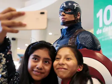 Dua penggemar wanita berselfie di dekat patung Captain America saat mengantre untuk menyaksikan pemutaran perdana film The Avengers: Endgame di La Paz, Bolivia (24/4). Film Avengers ini diputar perdana secara serentak pada 24 April 2019. (Reuters/David Mercado)