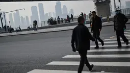 Orang-orang menyeberang jalan yang mengalir di sepanjang Sungai Yangtze di Wuhan (20/11/2020). Beberapa warga sudah tidak menggunakan masker saat melakukan aktivitas di luar ruangan. (AFP/Hector Retamal)