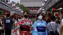 Dua wanita mengenakan yukata, pakaian musim panas tradisional Jepang mengunjungi kuil Buddha Sensoji di distrik Asakusa Tokyo (12/8/2021). Wanita biasanya mengenakan yukata dari bahan berwarna dasar cerah atau warna pastel dengan corak aneka warna yang terang. (AFP/David Gannon)