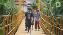 Anak-anak melintasi jembatan gantung Kuning yang menghubungkan Pasar Minggu Poltangan ke Cililitan Condet, Jakarta, Selasa (28/12/2021). Jembatan gantung Kuning dengan panjang 40 meter di atas sungai Ciliwung tersebut baru baru ini dijadikan lokasi foto untuk konten medsos. (merdeka.com/Imam Buhori)