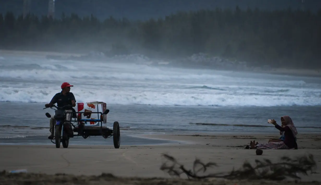 Penjual es krim mengendarai becak ketika seorang wanita berswafoto saat berlibur Lebaran di Pantai Lhoknga, Aceh Besar, Aceh, Minggu (9/6/2019). (CHAIDEER MAHYUDDIN/AFP)