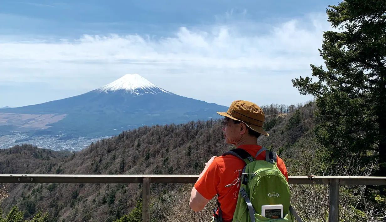 <p>Seorang pejalan kaki melihat Gunung Fuji dari pinggiran kota Fujiyoshida, prefektur Yamanashi, pada Kamis (22/4/021). Prefektur Yamanashi terletak di sebelah barat Tokyo yang memiliki spot-spot wisata terkenal, salah satunya gunung tertinggi di Jepang, Gunung Fuji. (Behrouz MEHRI / AFP)</p>