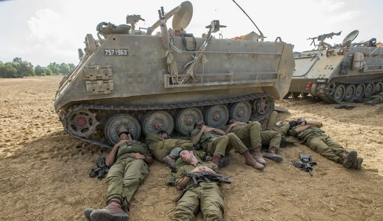 Pasukan Tentara Israel tidur di tanah di samping kendaraan lapis baja di perbatasan Israel dengan Jalur Gaza. (REUTERS / Nir Elias)
