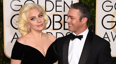 Lady Gaga ditemani Taylor Kinney menghadiri acara Golden Globes 2016 di Beverly Hilton Hotel, California, Minggu (10/1). Kompak mengenakan gaun bernuansa hitam, sang Mother Monster menggandeng mesra sang tunangan. (Jason Merritt/Getty Images/AFP)