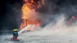 Petugas pemadam kebakaran menyemprotkan air untuk memadamkan tangki minyak yang terbakar di pelabuhan Es Sider, Libya, (6.1).  Kerusuhan yang terjadi di Libya membuat tangki minyak ini ditutup hampir lebih dari satu7 tahun. (REUTERS / Stringer)