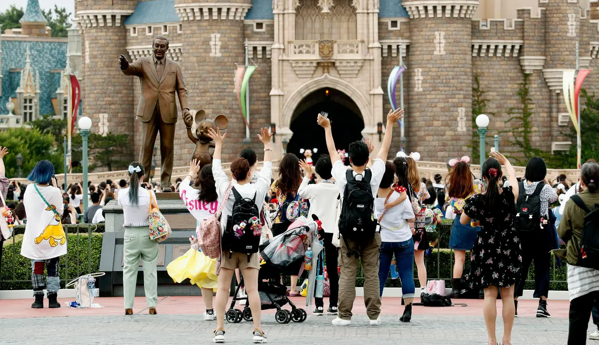 Pengunjung melambai tangan kepada karakter Disney yang tampil di Tokyo Disneyland di Urayasu, dekat Tokyo, Rabu (1/7/2020). Tokyo Disneyland dibuka kembali untuk pertama kalinya dalam empat bulan setelah sempat ditutup karena penyebaran Covid-19 . (Kyodo News via AP)