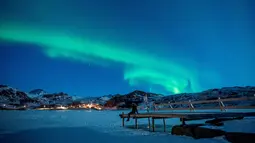 Seorang wanita duduk di dermaga untuk menonton Aurora Borealis atau Northern Lights di di Kepulauan Lofoten, Bostad, lingkaran Arktik, Norwegia, Sabtu (3/3). Cahaya Aurora biasa terlihat di sekitar daerah Kutub Utara dan Selatan. (Olivier MORIN/AFP)