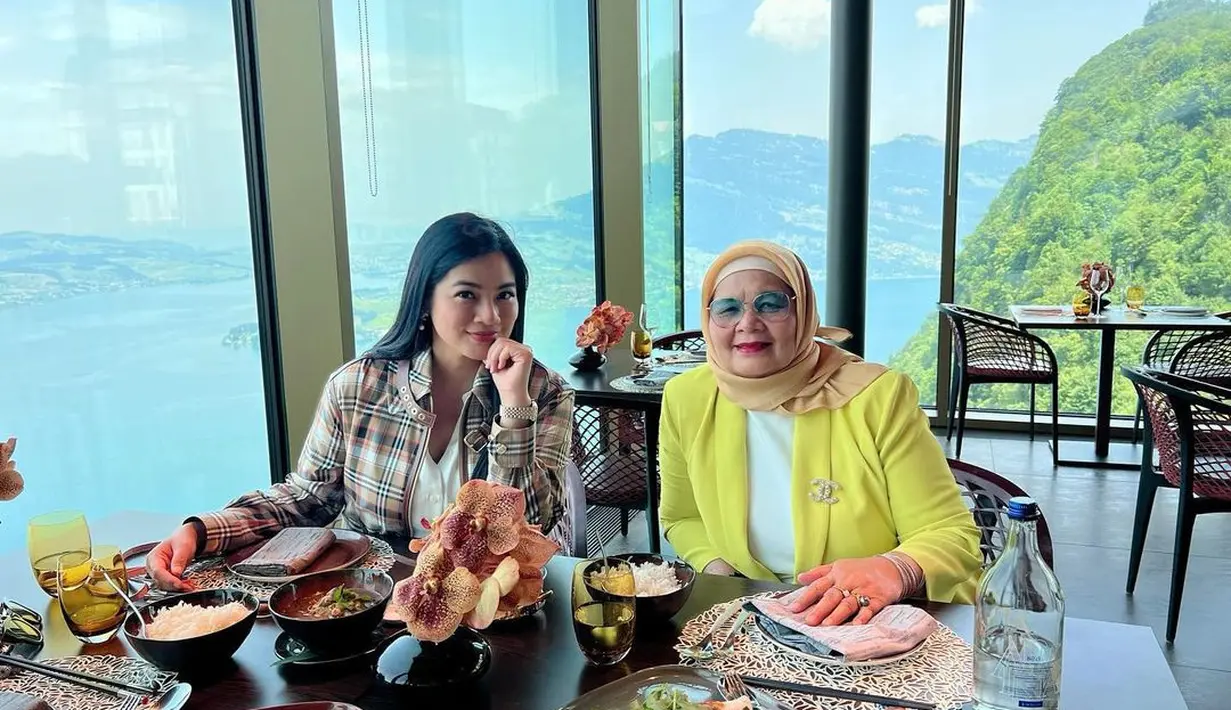 Titi Kamal bersama sang mama saat menikmati makan siang dengan latar belakang keindahan pemandangan sungai dan gunung di Swiss. (instagram/titi_kamall)