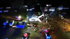 Gambar udara memperlihatkan kendaraan darurat berada dekat lokasi jatuhnya pesawat kecil Cessna 208 yang menabrak hanggar lapangan terbang di Desa Chrcynno, dekat Warsawa, Polandia, Senin (17/7/2023). Insiden tersebut lantas menewaskan lima orang. (Damien SIMONART/AFP)