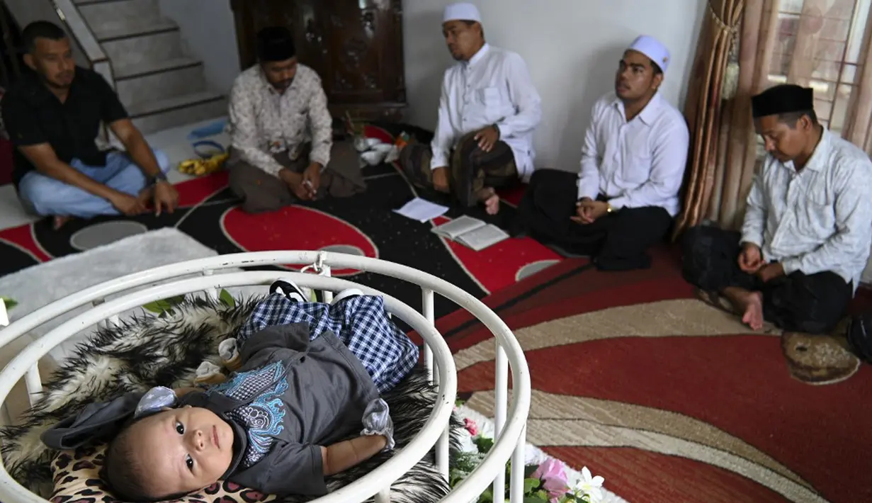 Orang-orang berdoa untuk bayi yang baru lahir saat prosesi aqiqah di Banda Aceh, Aceh, 4 November 2021. Aqiqah adalah tradisi menyambut bayi yang baru lahir dalam agama Islam. (CHAIDEER MAHYUDDIN/AFP)