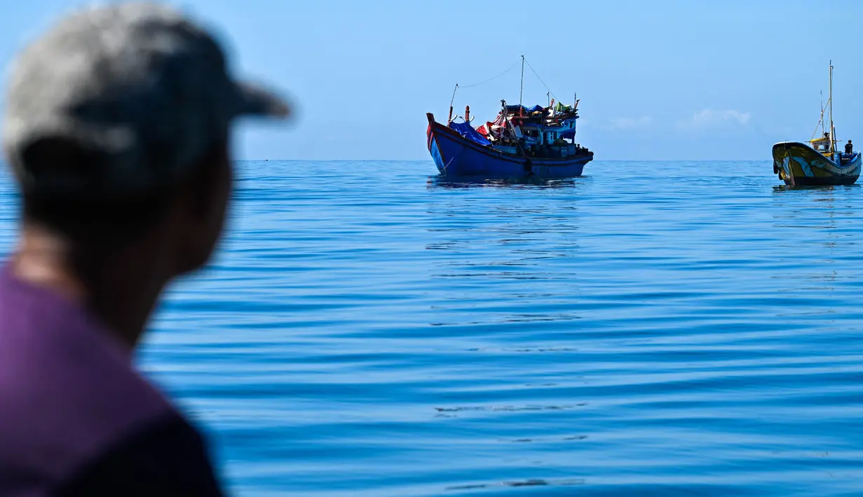 Seorang pria di atas kapal melihat para pengungsi Rohingya yang berlabuh di lepas pantai Labuhan Haji, Aceh Selatan, pada Selasa 22 Oktober 2024. (CHAIDEER MAHYUDDIN/AFP)