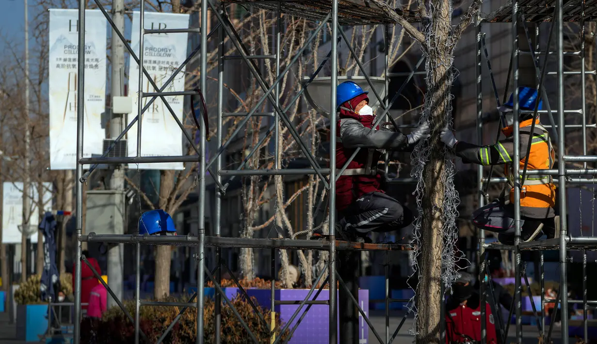 Pekerja yang mengenakan masker sedang memasang lampu pada pohon untuk perayaan Tahun Baru mendatang di distrik perbelanjaan Wangfujing, Beijing, China, Rabu (14/12/2022). Mulai hari ini, Komisi Kesehatan Nasional China melaporkan penurunan kasus harian COVID-19 sejak pemerintah melonggarkan pengujian PCR setelah kasus harian mencapai rekor tertinggi. (AP Photo/Andy Wong)