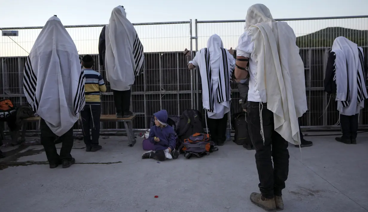 Orang-orang Yahudi Ultra Ortodoks yang ditutupi selendang berdoa saat perayaan liburan Lag BaOmer di situs makam tradisional Rabbi Shimon Bar Yochai di Gunung Meron, Israel, Kamis (19/5/2022). Orang Israel menyalakan api unggun selama perayaan Lag BaOmer untuk memperingati berakhirnya wabah yang dikatakan telah memusnahkan orang Yahudi di zaman Romawi. (AP Photo/Ariel Schalit)