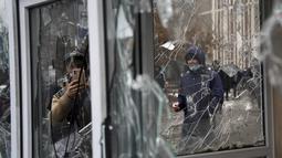 Seorang pria mengambil foto dari jendela kios polisi yang dirusak oleh demonstran selama protes di Almaty, Kazakhstan, Rabu (5/2/2022). Demonstran yang menolak kenaikan harga gas cair bentrok dengan polisi di kota terbesar Kazakhstan dan mengadakan protes di sekitar kota. (AP Photo/Vladimir Tretyako