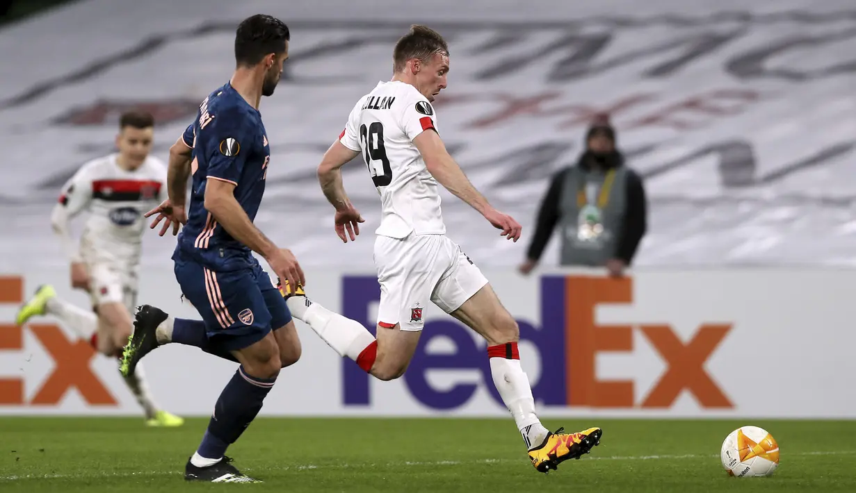 Penyerang Dundalk, David McMillan berebut bola dengan bek Arsenal, Pablo Mari dalam pertandingan Grup B Liga Europa 2020/2021 di Stadion Aviva, Jumat (11/12/2020) dini hari WIB. Arsenal menang 4-2 saat bertandang di markas wakil Irlandia, Dundalk. (Brian Lawless/PA via AP)