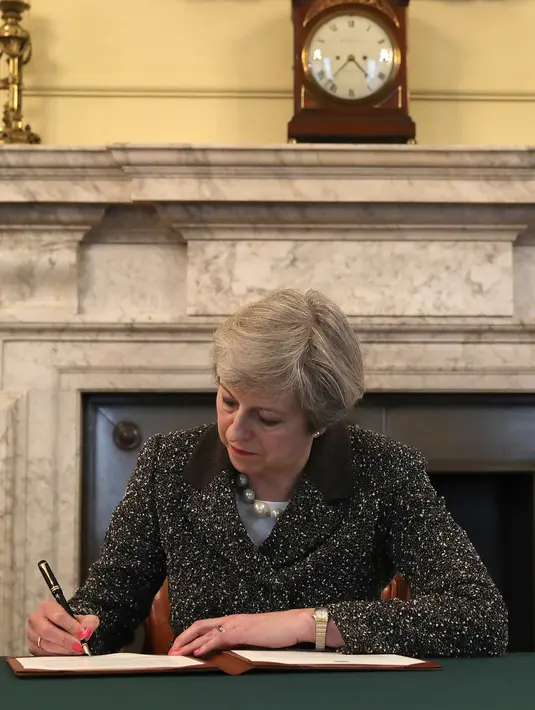 PM Inggris Theresa May saat akan menandatangani surat permohonan Artikel 50 di 10 Downing Street, London, Selasa (28/3). Penandatangan ini secara resmi memulai proses keluarnya Inggris dari keanggotaan Uni Eropa atau Brexit. (Christopher Furlong/Pool/AFP)
