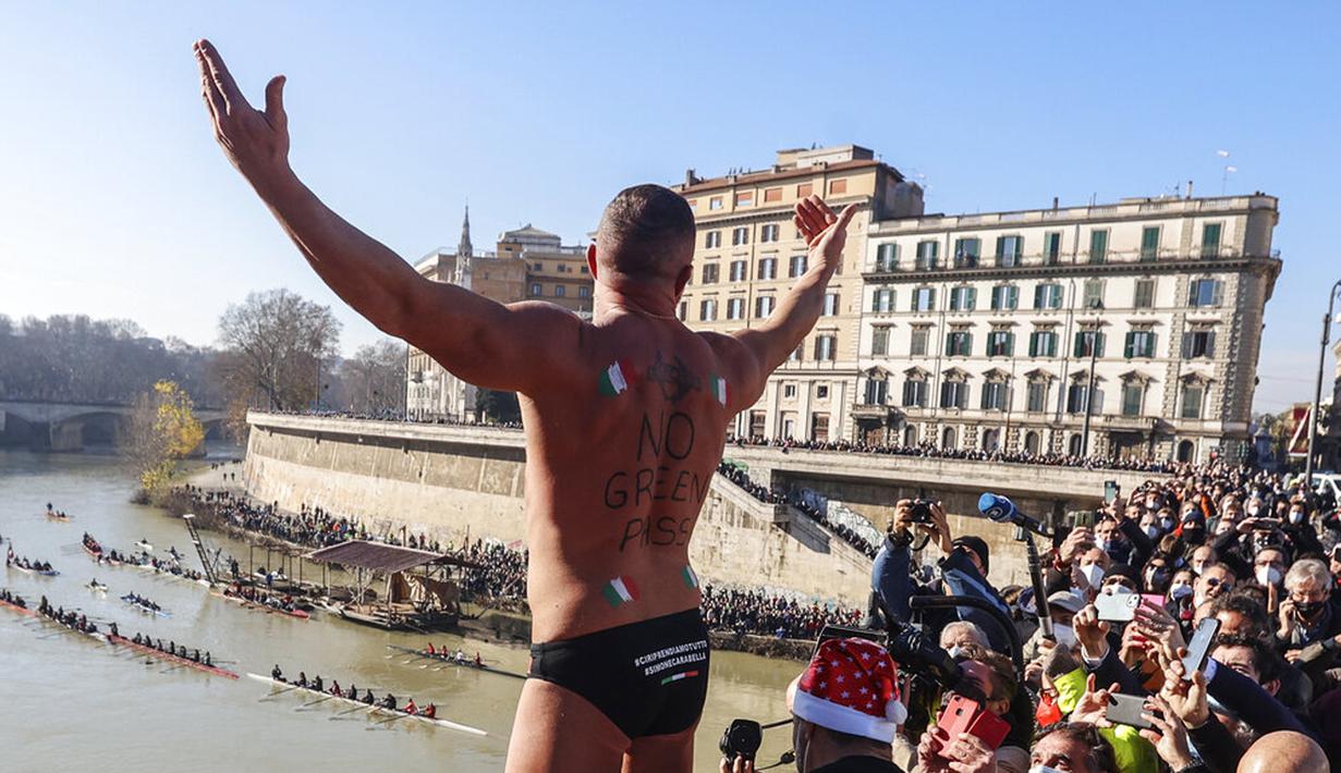 Simone Carabella dari Italia dengan slogan 'No Green Pass' terlukis pada punggungnya menyapa orang-orang saat dia bersiap untuk melompat ke Sungai Tiber dari Jembatan Cavour setinggi 18 meter (59 kaki) untuk merayakan Tahun Baru di Roma, 1 Januari 2022. (AP Photo/Riccardo De Luca)