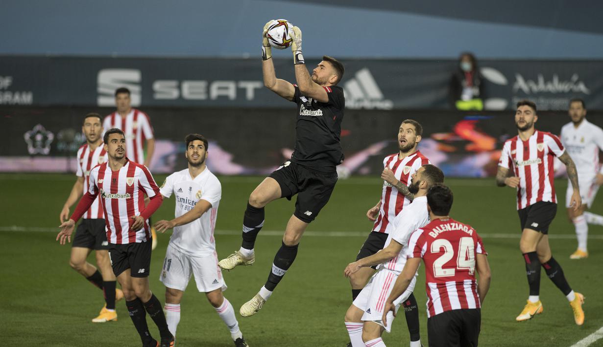 Kiper Athletic Bilbao, Unai Simon (tengah) menangkap bola dari ancaman pemain Real Madrid dalam laga semifinal Piala Super Spanyol 2020/21 di La Rosaleda Stadium, Malaga, Kamis (14/1/2021). Athletic Bilbao menang 2-1 atas Real Madrid. (AFP/Jorge Guerrero)