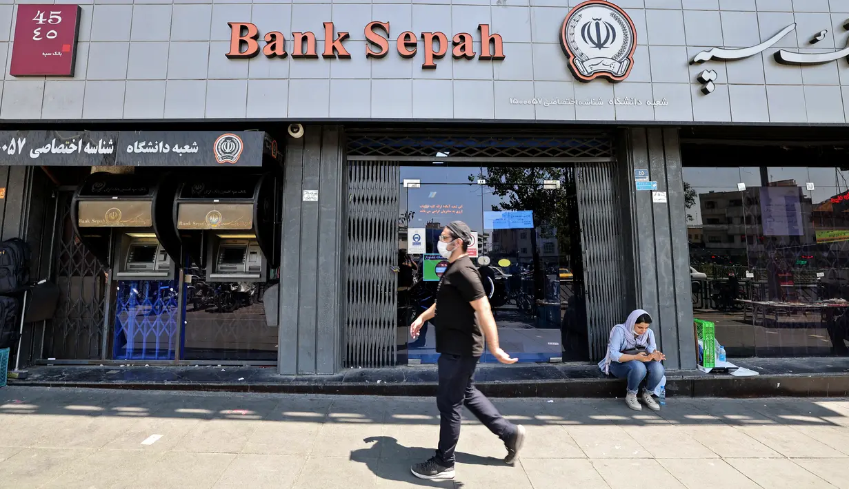 Seorang pria Iran yang mengenakan masker berjalan melewati cabang Bank Sepah yang tutup di pusat kota Teheran, Selasa (20/7/2021). Iran memberlakukan lockdown di ibu kota Teheran dan provinsi terdekat setelah kasus infeksi Covid-19 mencapai rekor tertingginya selama wabah kelima. (ATTA KENARE/AFP)