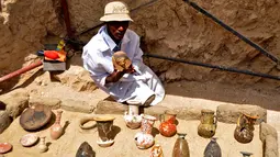 Seorang arkeolog Mesir memperlihatkan sejumlah artefak yang ditemukan di sebuah pemakaman berumur 3.500 tahun, sebelah selatan kota Luxor, Selasa (18/4). Kuburan yang ditemukan di Draa Abul Nagaa itu diperkirakan berasal dari Dinasti ke-18. (STRINGER/AFP)