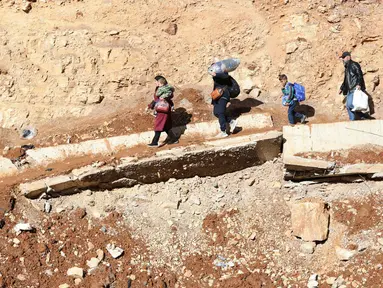 Orang-orang yang melarikan diri dari invansi militer Israel di Lebanon menyeberangi sebuah kawah, yang disebabkan oleh serangan Israel, di daerah Masnaa, salah satu wilayah yang berbatasan langsung dengan Suriah, pada 20 November 2024. (Anwar AMRO/AFP)