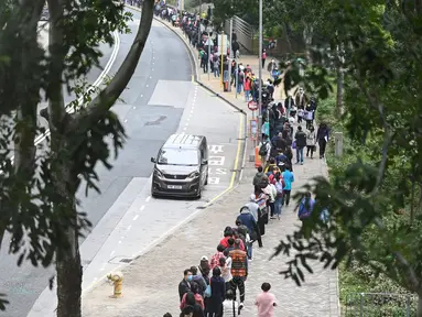 Orang-orang mengantre di stasiun pengumpulan spesimen bergerak untuk pengujian Covid-19 di distrik Tung Chung, Hong Kong pada 10 Februari 2022. Antrean terjadi ketika pihak berwenang bergegas untuk meningkatkan kapasitas pengujian menyusul rekor jumlah infeksi baru yang tinggi. (Peter PARKS / AFP)