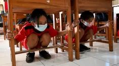 Anak-anak sekolah berlindung di bawah meja untuk melindungi diri mereka sat latihan gempa dan tsunami di Tanjung Benoa, Kabupaten Badung, Bali, 24 Mei 2022. (SONY TUMBELAKA/AFP)