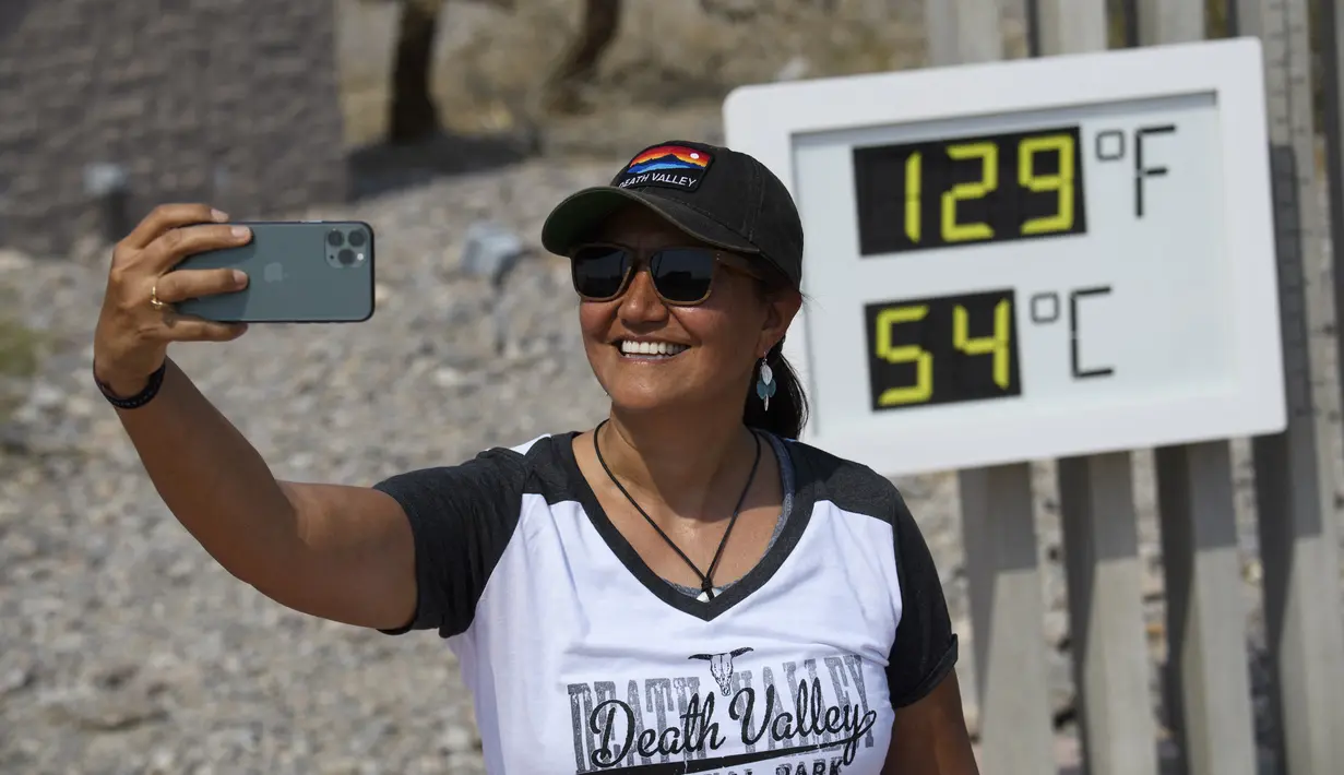 Karina Simpson berswafoto dengan termometer yang menunjukkan suhu 54 Derajat Celcius di Pos Pusat Pengunjung Furnace Creek di Taman Nasional Death Valley, California, Kamis (17/6/2021). Sebagian besar AS bagian barat bersiap menghadapi rekor gelombang panas minggu ini. (Patrick T. FALLON/AFP)