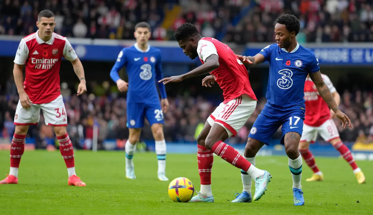 Pemain Arsenal Thomas Partey (tengah) berebut bola dengan pemain Chelsea Raheem Sterling pada pertandingan sepak bola Liga Inggris di Stadion Stamford Bridge, London, Inggris, 6 November 2022. Arsenal kembali memuncaki klasemen Liga Inggris usai mengalahkan Chelsea dengan skor 1-0. (AP Photo/Kirsty Wigglesworth)