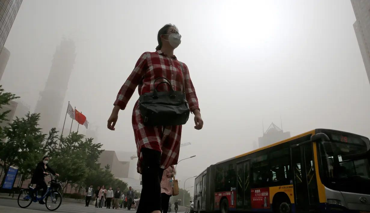 Seorang wanita berjalan sambil mengenakan masker saat badai debu menerjang kota Beijing, China, Kamis (4/5). Badai debu membuat otoritas memerintahkan orang tua dan anak-anak untuk tetap berada dalam ruangan. (AP Photo/Andy Wong)