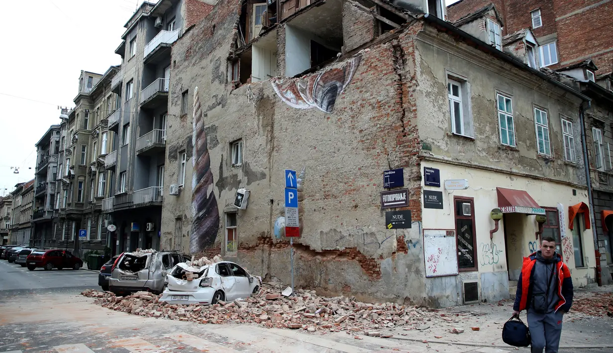 Seorang pria berjalan melewati sebuah bangunan yang rusak dan mobil-mobil hancur oleh puing-puing setelah gempa di jalan-jalan pusat kota Zagreb (22/3/2020).  Gempa magnitudo 5,3 ini tercatat sebagai yang terbesar, yang mempengaruhi Kroasia dalam 140 tahun. (AFP/Damir Sencar)