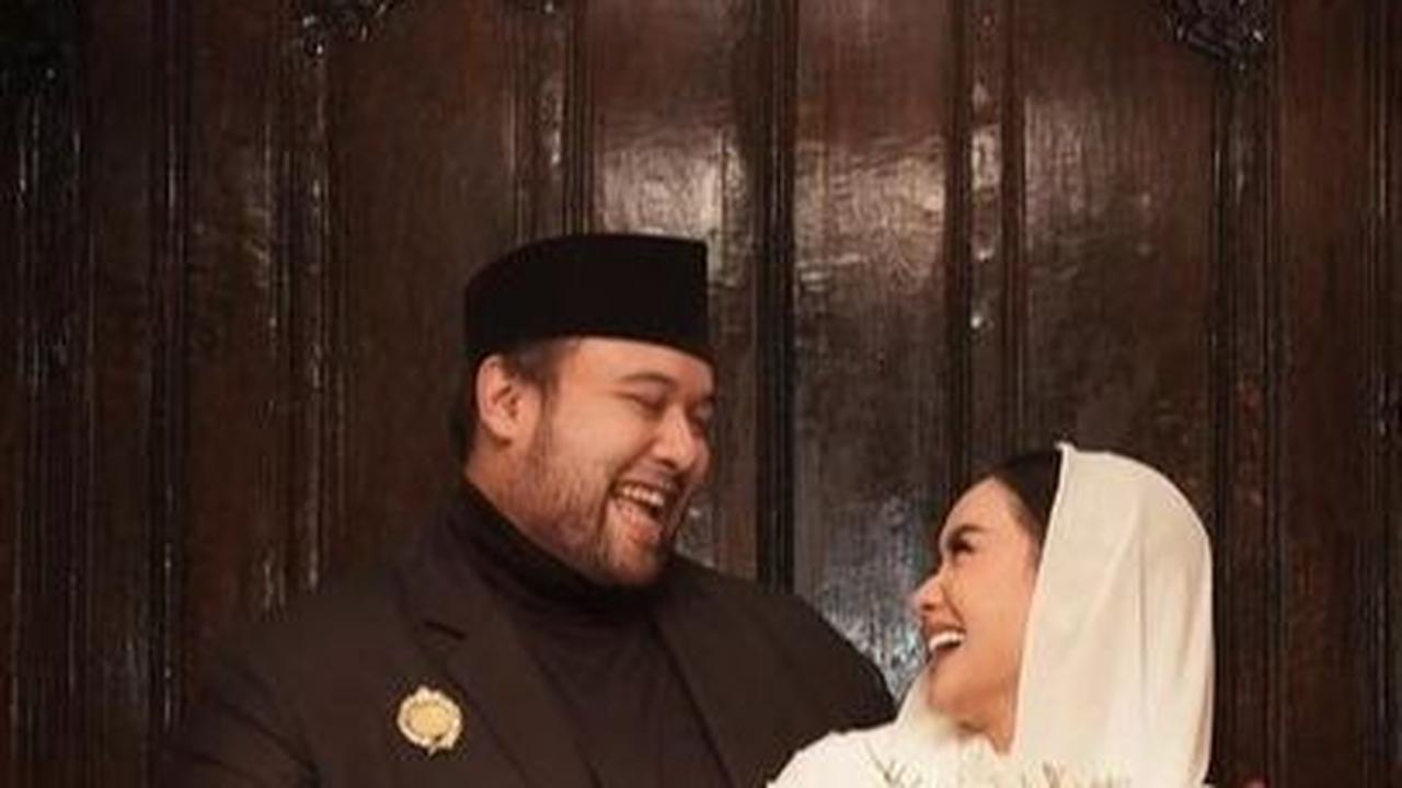 Didi terlihat gagah dengan peci dan jasnya. Sedangkan Cita tampak anggun dengan kebaya dan kerudung yang simpel. Di belakang mereka ada hiasan bunga cantik sebagai latar foto.