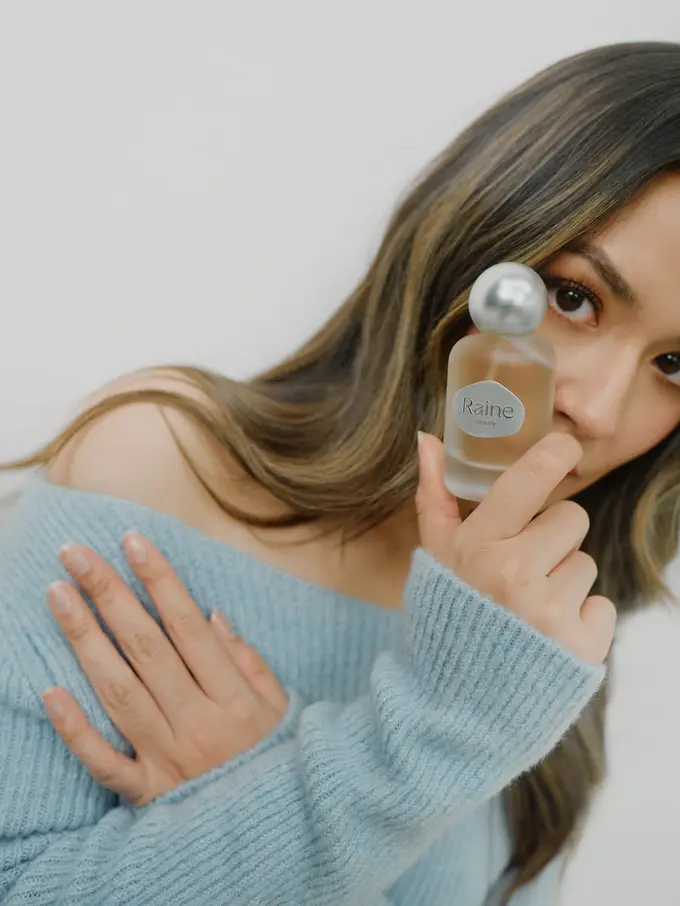Ilustrasi Raisa Memegang Parfum Ambivert/Raine Beauty