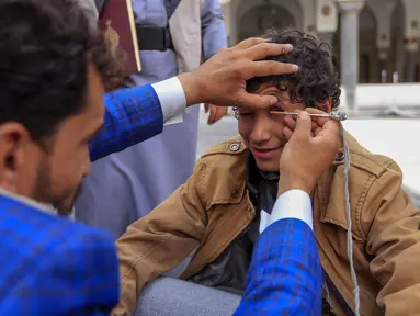 Seorang pria Yaman mengoleskan kosmetik tradisional Kohl ke kelopak mata remaja selama bulan puasa Ramadhan di Masjid Sanaa (16/4/2021).  Di Yaman, salah satu tradisi khas menandai Ramadhan yang masih lestari adalah aksi para pemuda yang merias mata dengan kohl. (AFP/ Mohammed Huwais)