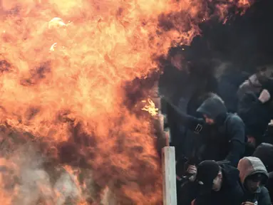 Suporter Ajax Amsterdam mencoba untuk melindungi diri dari ledakan bom molotov selama bentrokan dengan polisi anti huru-hara Yunani sebelum pertandingan Liga Champions melawan AEK Athena di Stadion Olimpiade Athena, Selasa (27/11). (Aris Messinis/AFP)