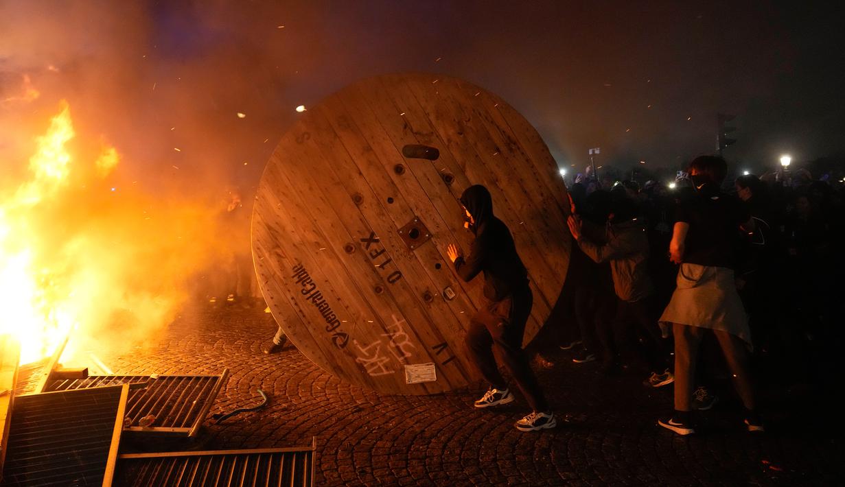 Demonstran menggulung gulungan kabel kayu ke barikade yang terbakar saat protes RUU Pensiun di Paris, Prancis, Jumat (17/3/2023). (AP Photo/Lewis Joly)