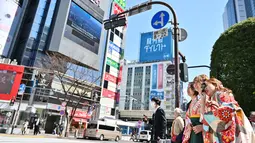 Seorang wanita berpakaian kimono (kanan) mengambil foto saat dirinya dan yang lain menunggu untuk menyeberangi persimpangan pejalan kaki yang terkenal di distrik Shibuya, Tokyo pada 20 Maret 2019. (Photo by CHARLY TRIBALLEAU / AFP)