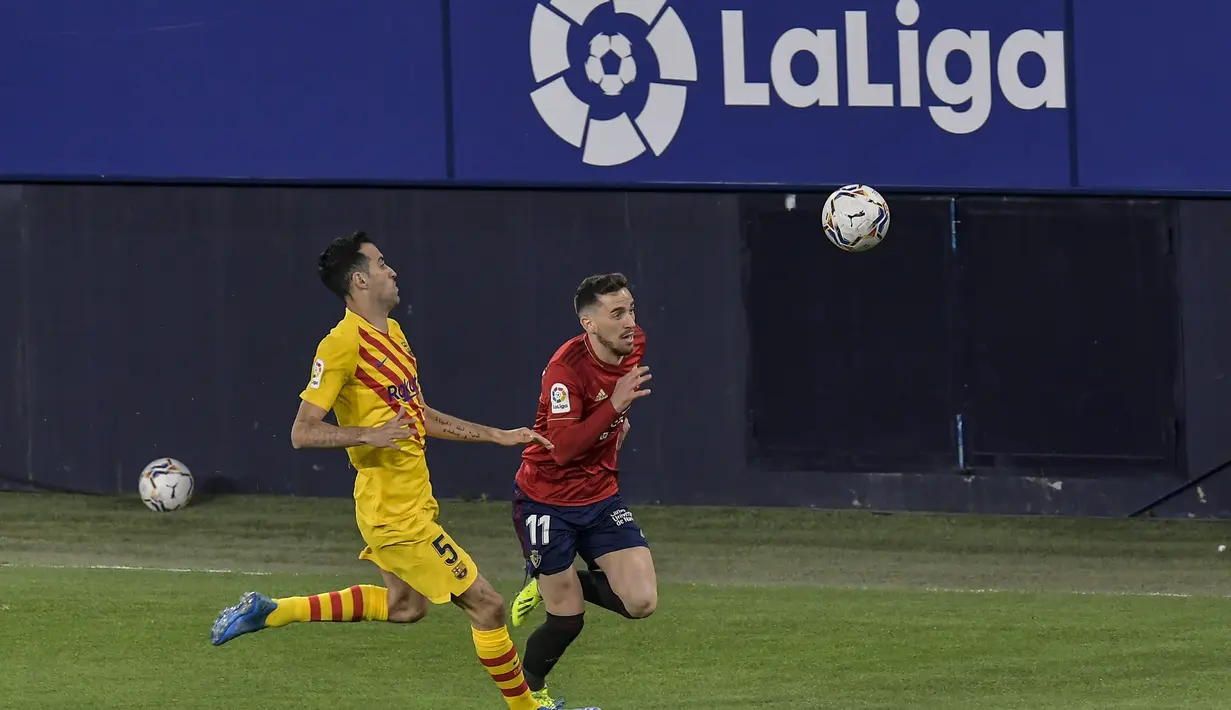 Penyerang Osasuna, Kike Barja membawa bola dari kejaran gelandang Barcelona, Sergio Busquets pada pertandingan lanjutan La Liga Spanyol di stadion El Sadar di Pamplona, Minggu (7/3/2021). Barcelona sukses menjaga jarak dua poin dengan pemuncak klsemen Atletico Madrid. (AP Photo/Alvaro Barrientos)