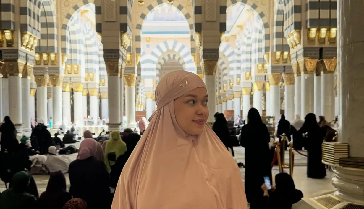 Sementara itu pada potret terakhir di dalam masjid, ia mengenakan busana syari berwarna peach pastel yang memancarkan aura feminin dan lembut. Warna tersebut memantulkan cahaya interior dengan cantik sehingga wajahnya terlihat glowing alami. Model khimar yang rapi dengan detail minimal membuat tampilannya semakin dewasa dan anggun.  [@rklopper].